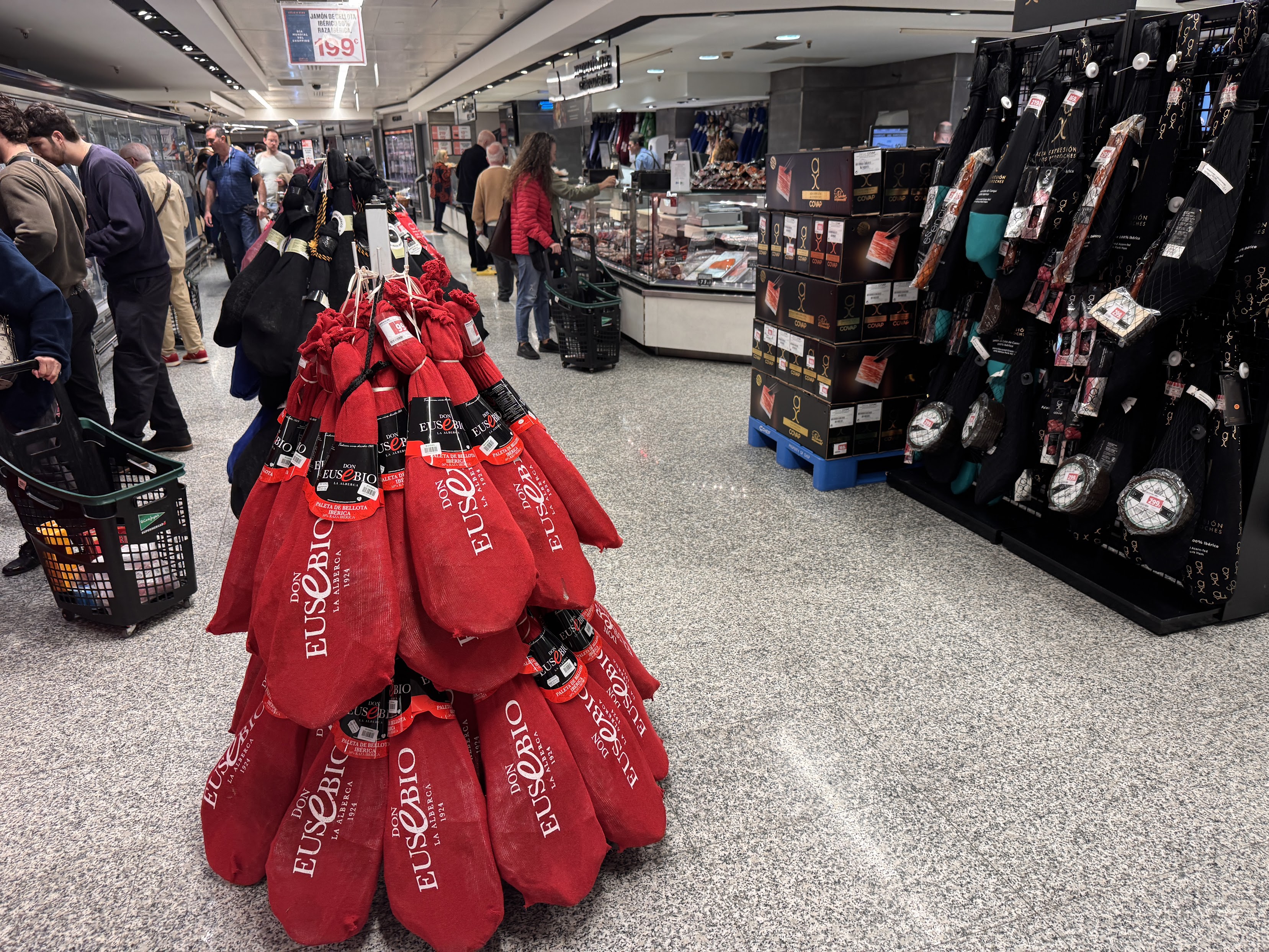 Interior of El Corte Inglés with red burlap-wrapped jamón products stacked near the entrance