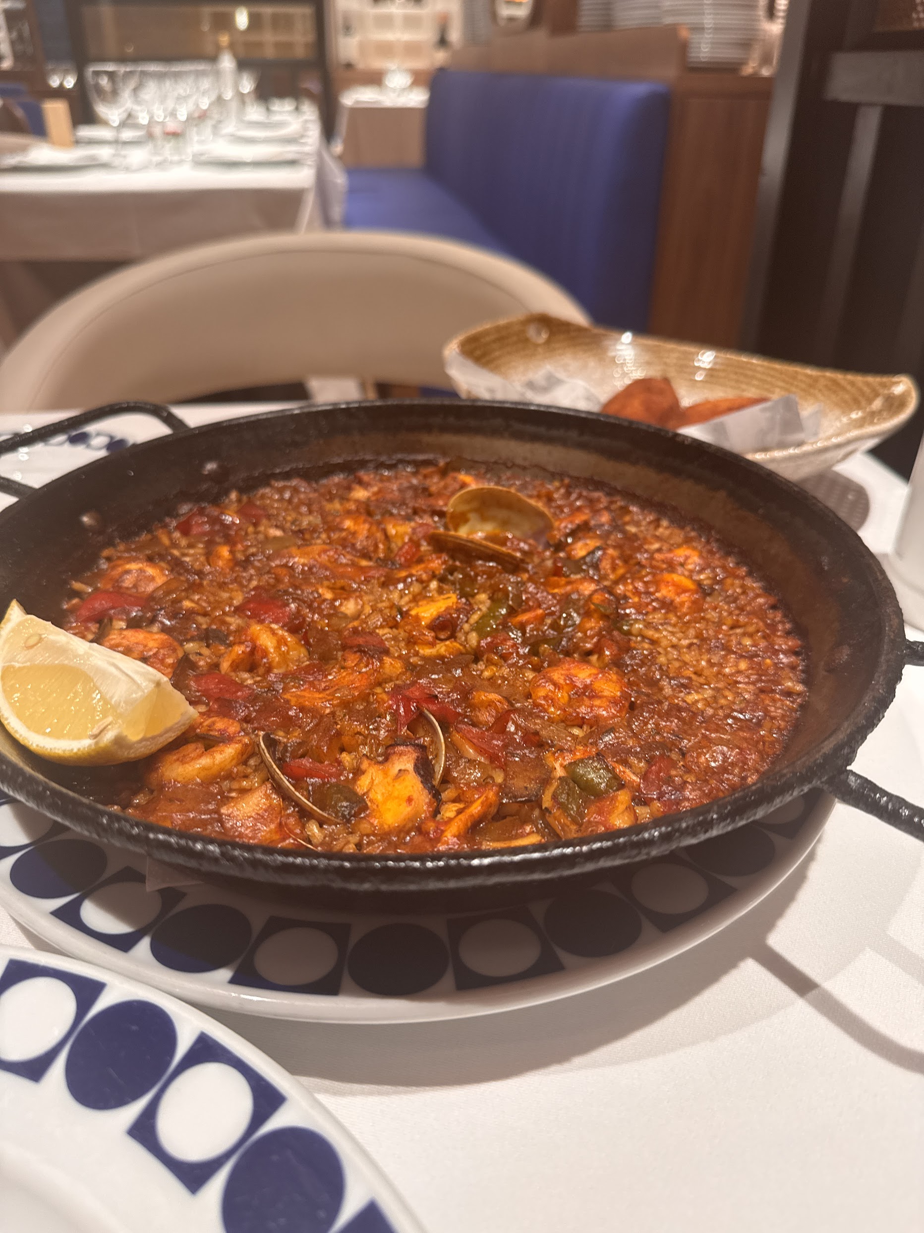 A wide iron pan of seafood paella with prawns, mussels and squid, garnished with lemon wedges, on a white tablecloth