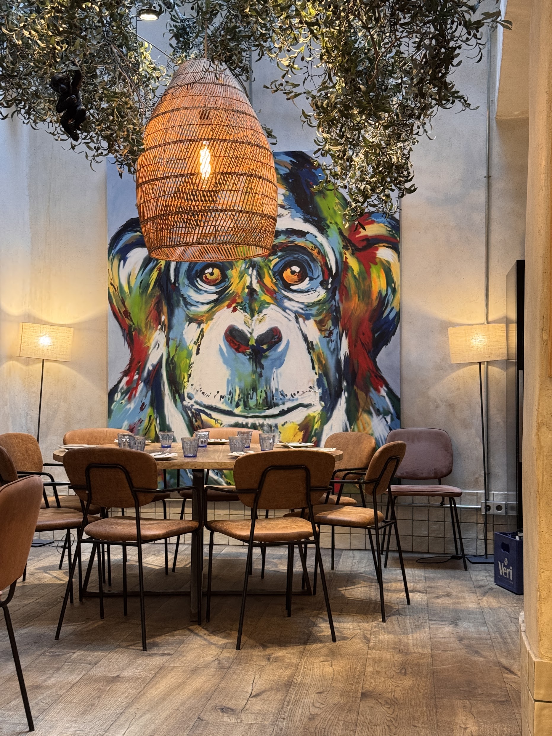 Restaurant interior with colorful chimp mural on the back wall, rattan pendant lamps, and olive branch decor