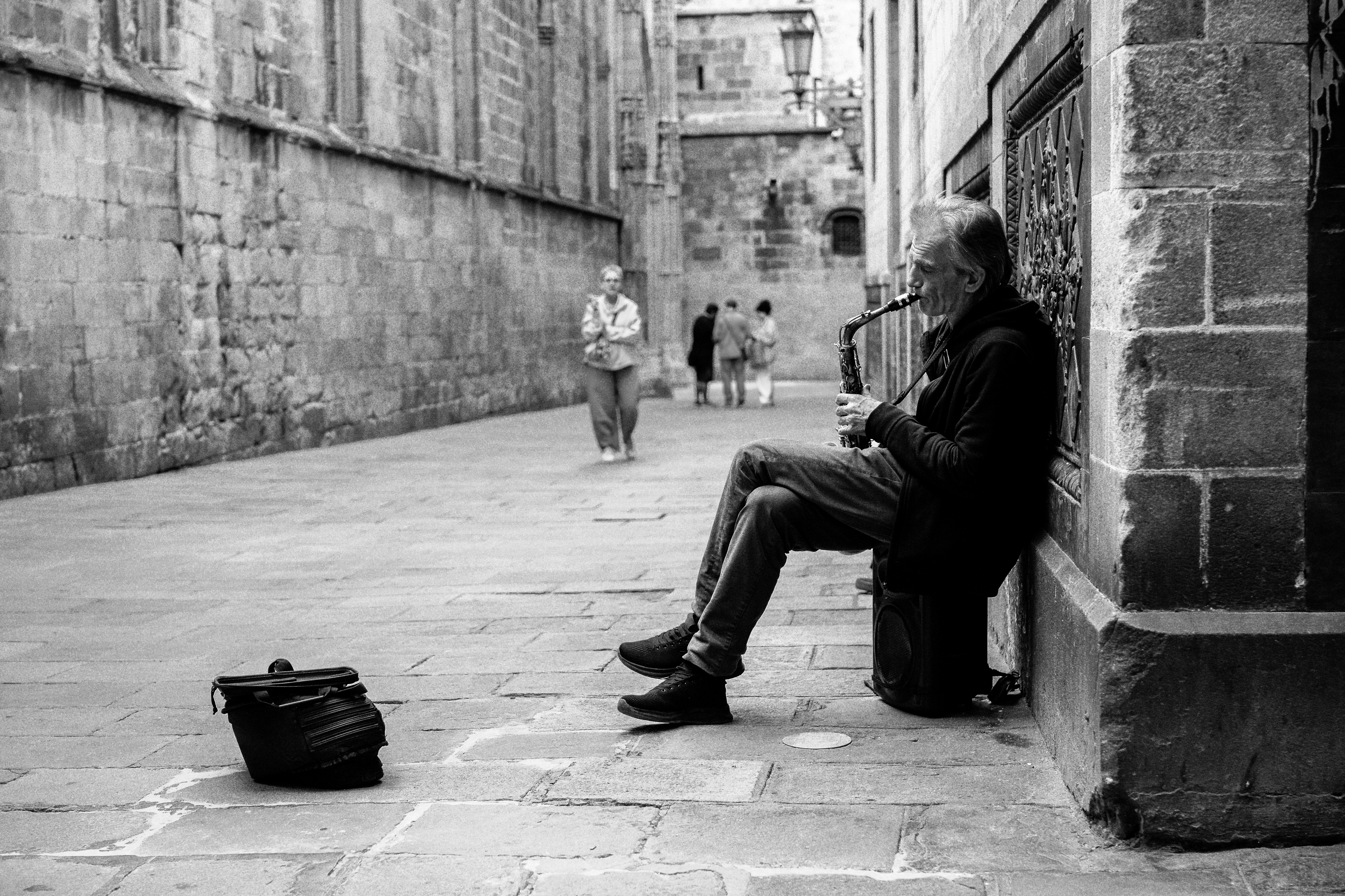 A saxophonist leans against a worn limestone wall in the Gothic Quarter, eyes closed mid-performance
