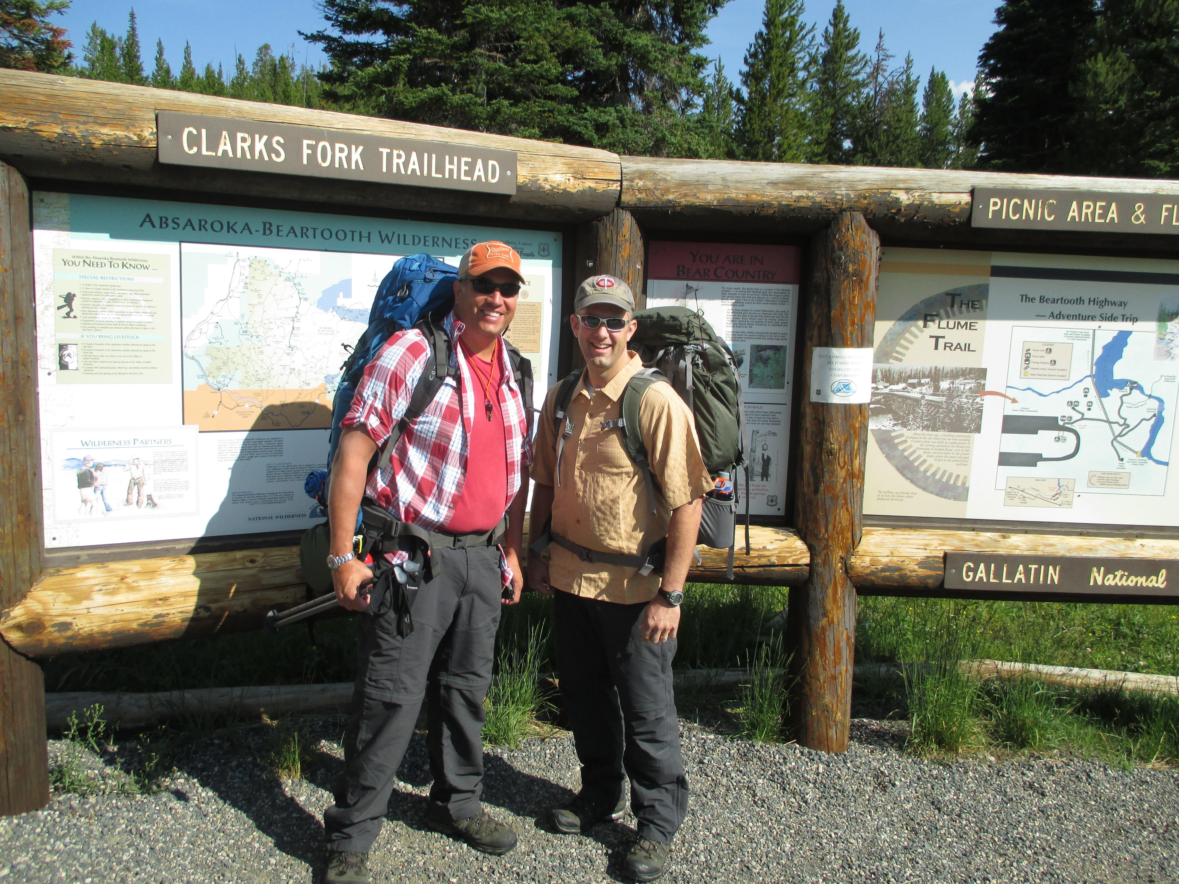 Two hikers with full packs at the Clarks Fork Trailhead sign in the Absaroka-Beartooth Wilderness