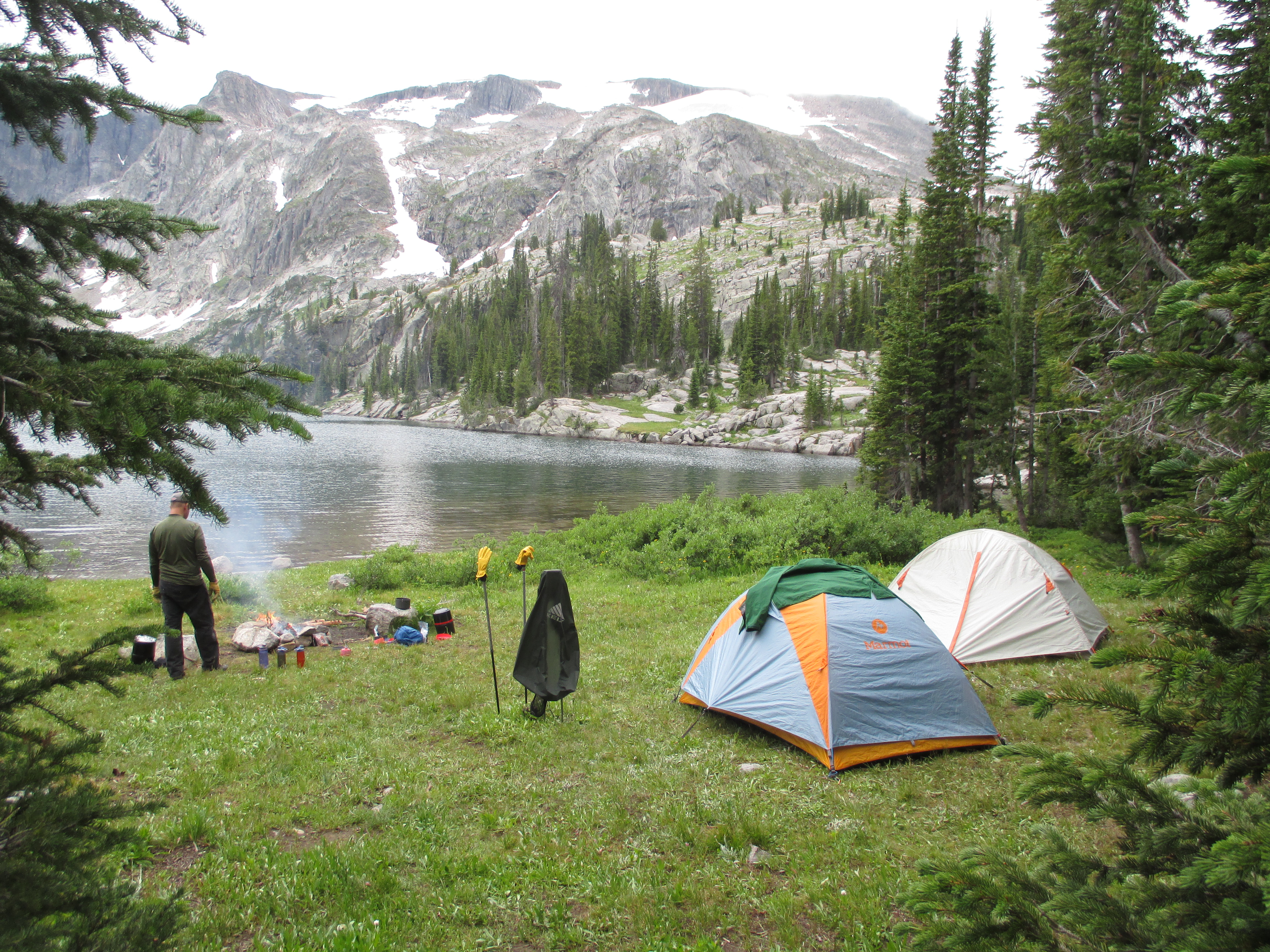 Camp at Dewey Lake with a fire burning, tents pitched on the grass, and 11,000-foot peaks rising over the water