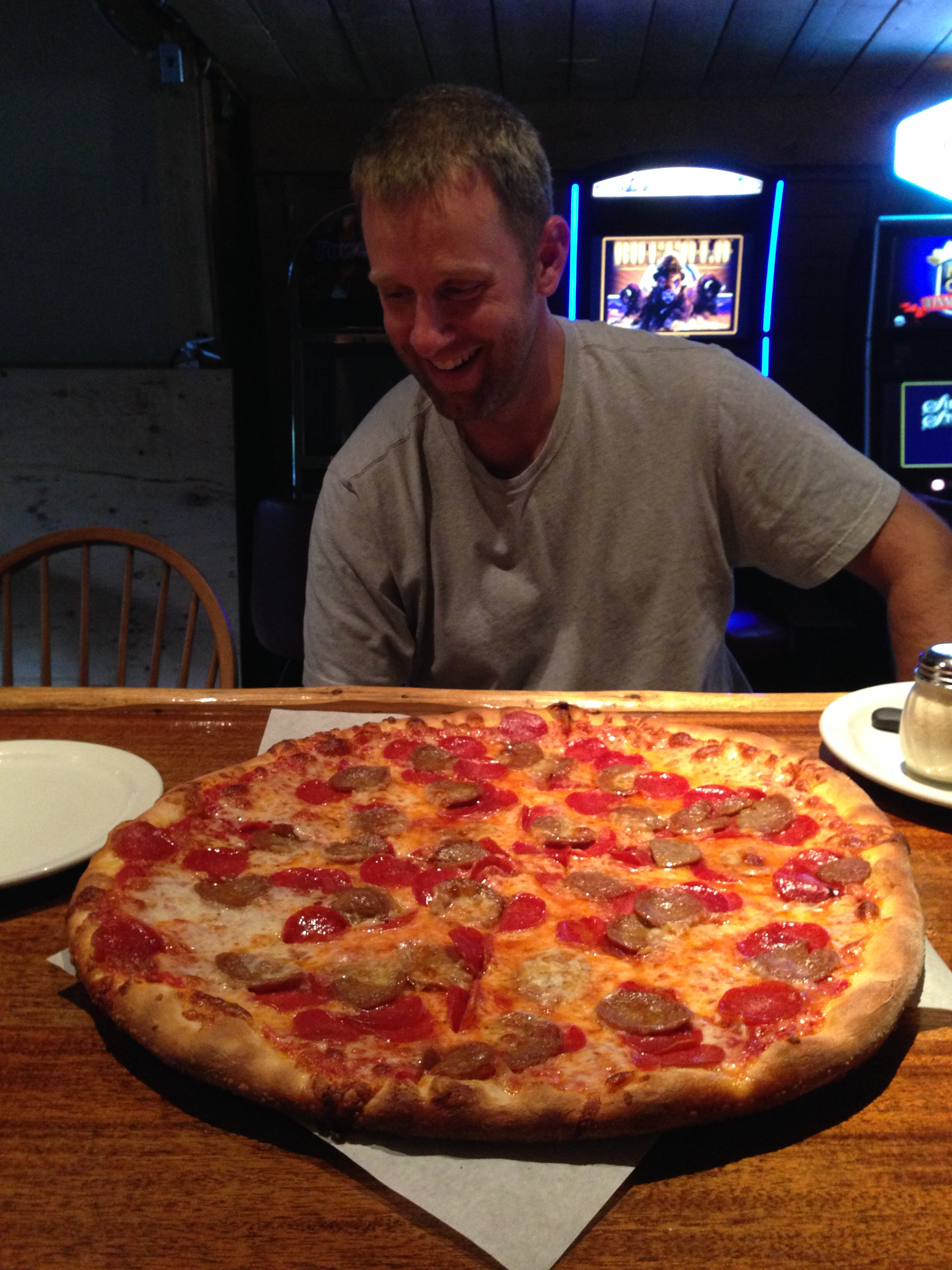 A laughing hiker sitting in front of an improbably large pepperoni and sausage pizza at the Miners Saloon in Cooke City