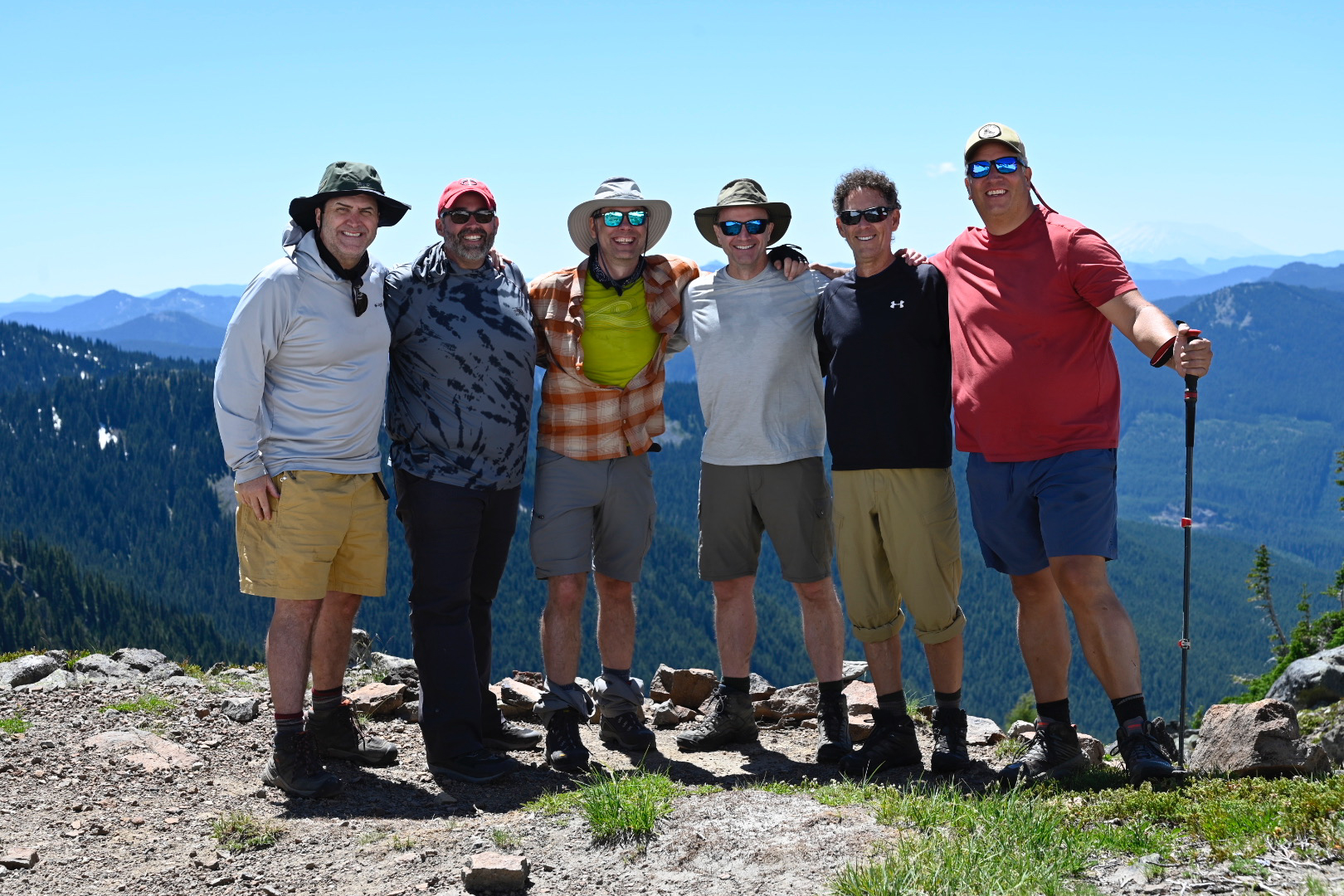 Group of six hikers on the rocky summit of High Rock Lookout, Cascade peaks stretching to the horizon under a clear blue sky