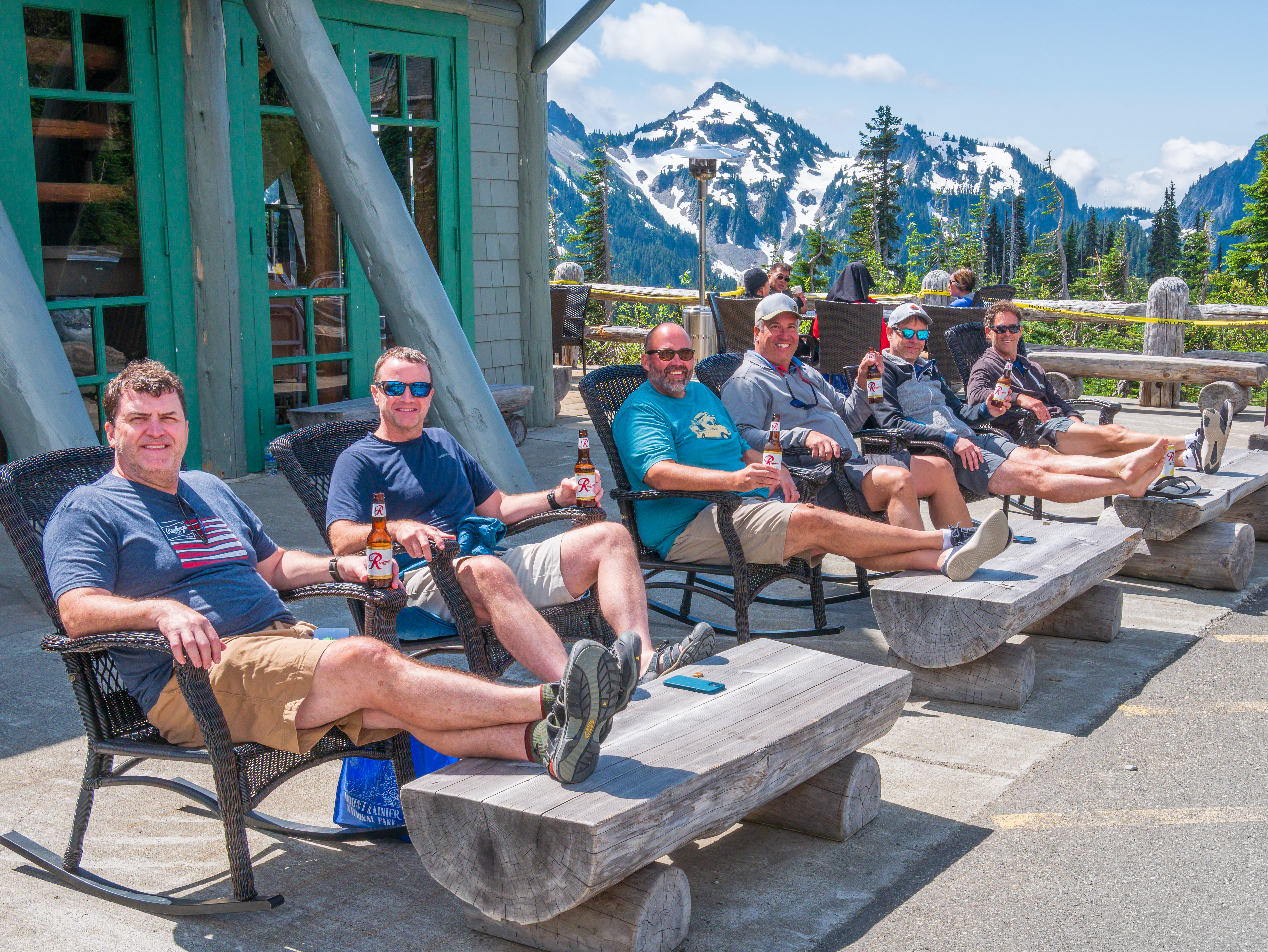 Group relaxing in chairs on the Paradise Lodge patio at Mount Rainier National Park, Rainier beer in hand, Tatoosh Range peaks rising behind