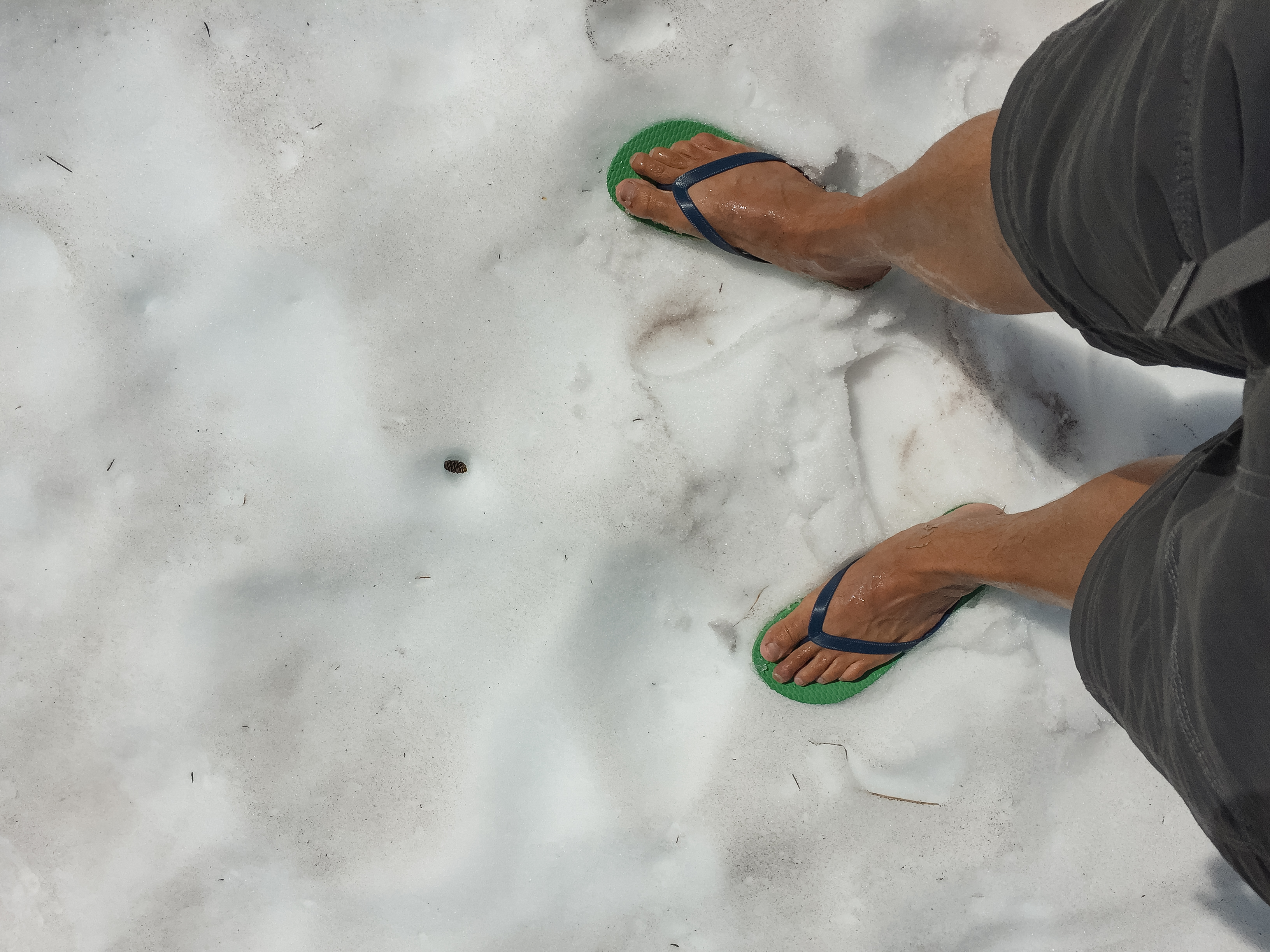 Feet in green flip-flops standing on snow at the Pelton Basin camp